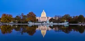 The west face of the US Capitol at dawn reflecting in the Capitol Reflecting Pool. Autumn foliage.